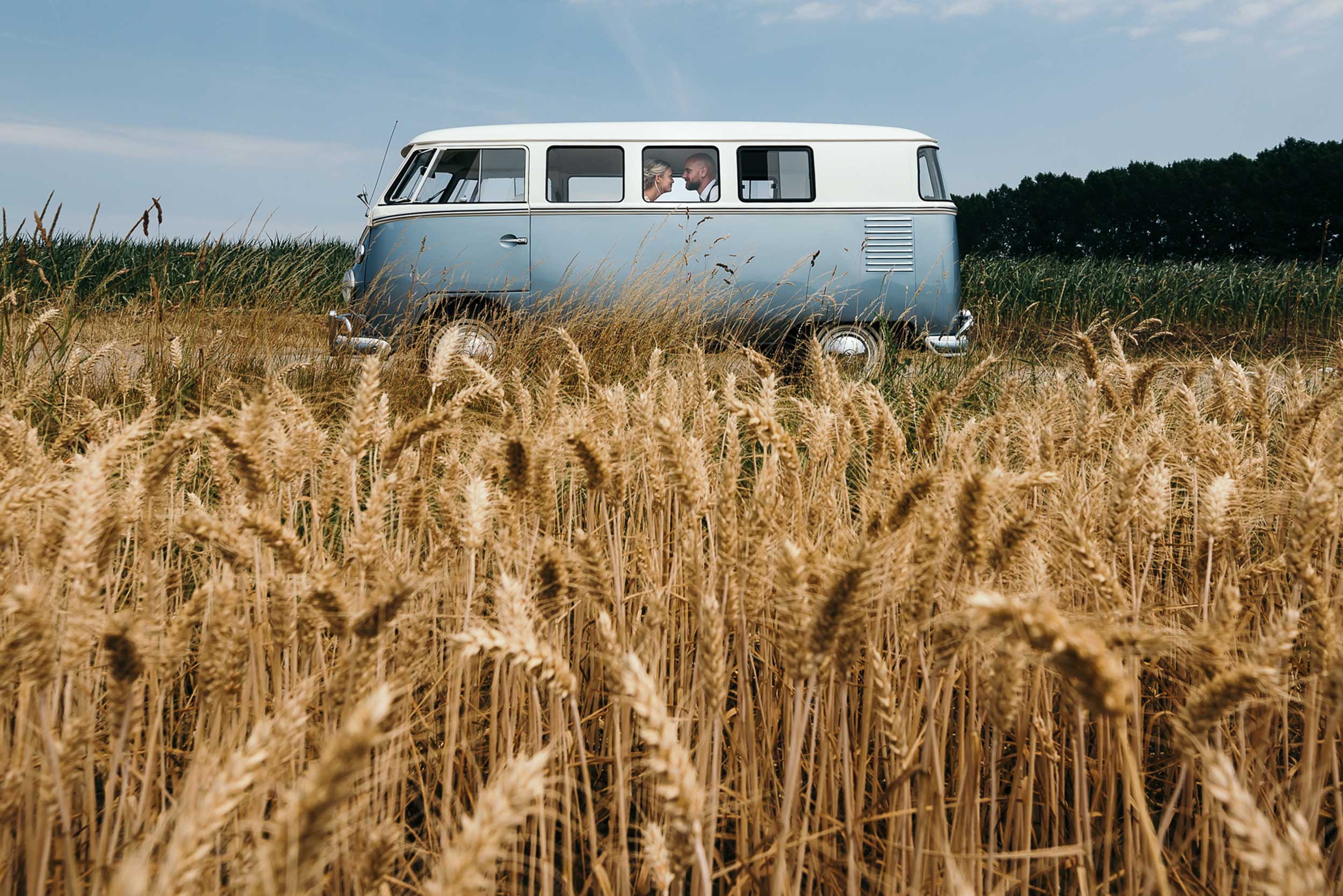 Sfeervolle Retrosfeer: Bruidspaar straalt in een retro Volkswagenbusje te midden van een idyllisch korenveld.