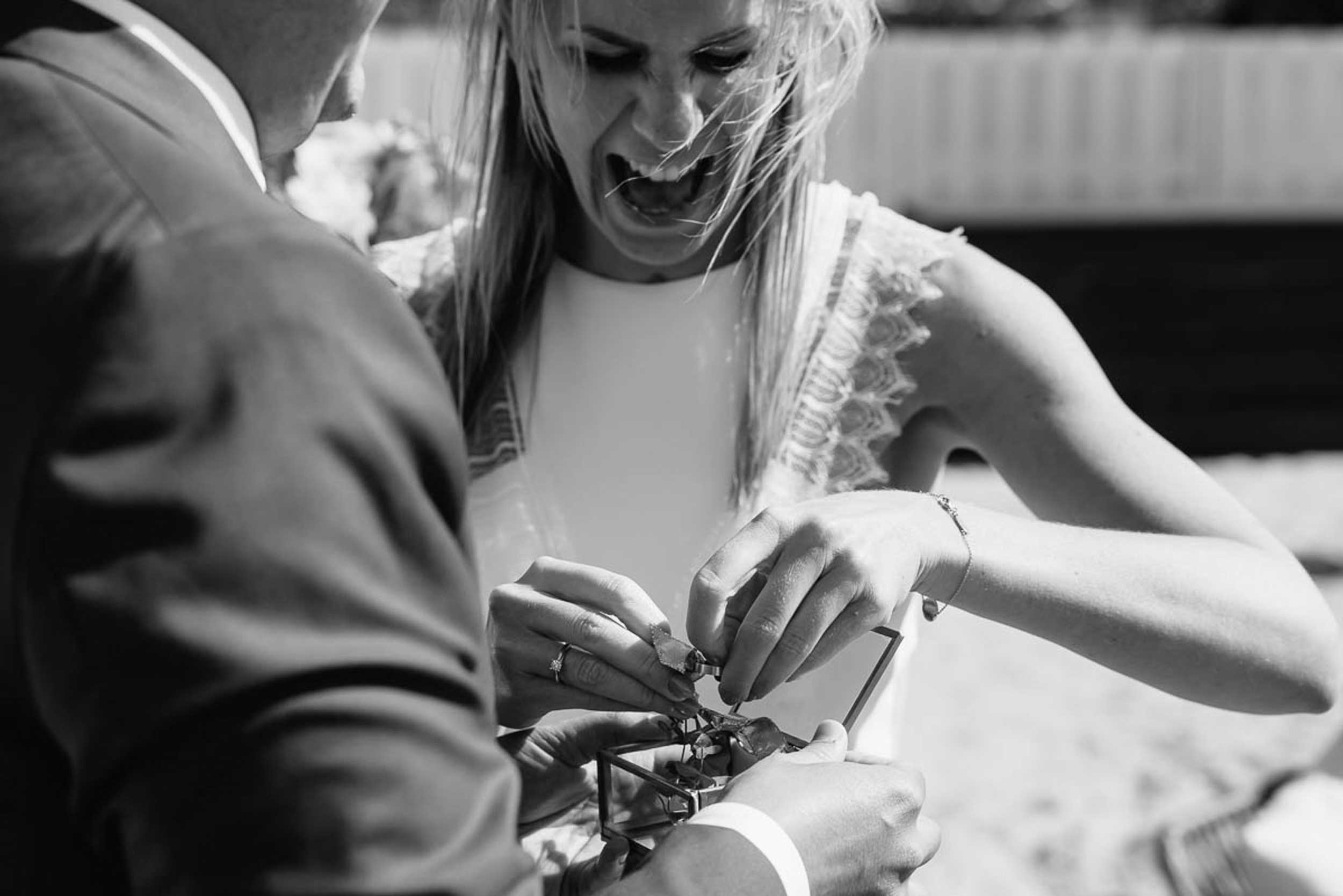 Zwart-wit beeld van de bruid die met expressie de ringen losmaakt uit een juwelendoosje.