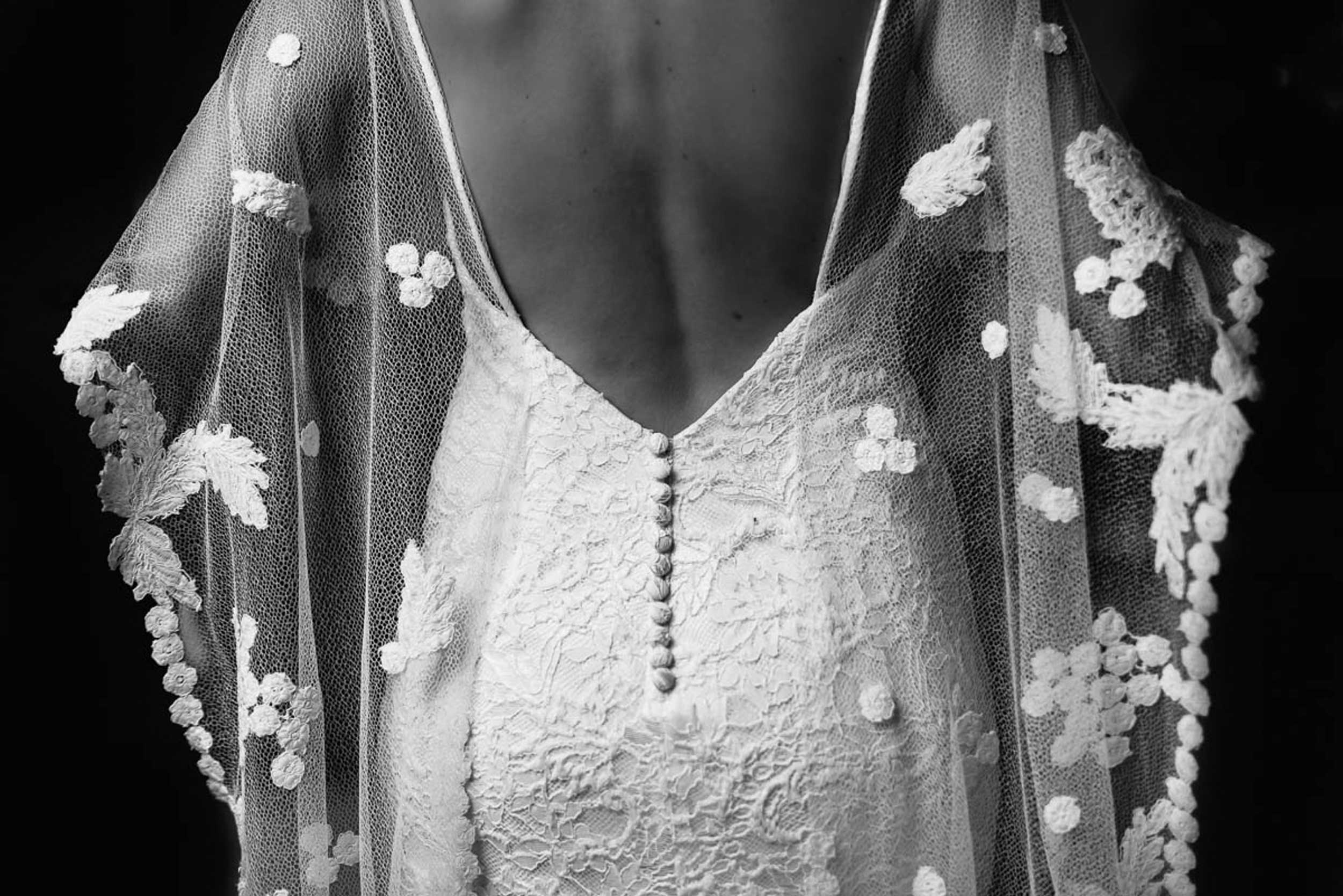 Fascinerend Detail: Prachtig zwart-wit beeld van het bruidskleed, losjes hangend om de schouders, fel afstekend tegen de donkere achtergrond.