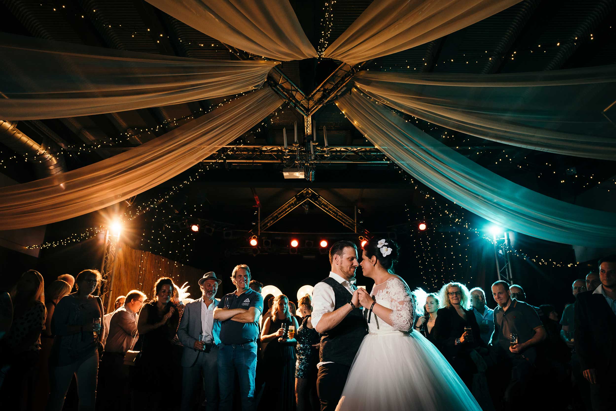 Magisch Moment: Topfoto van openingsdans, waar het bruidspaar fel afsteekt tegen de professioneel uitgelichte achtergrond in levendige kleuren.