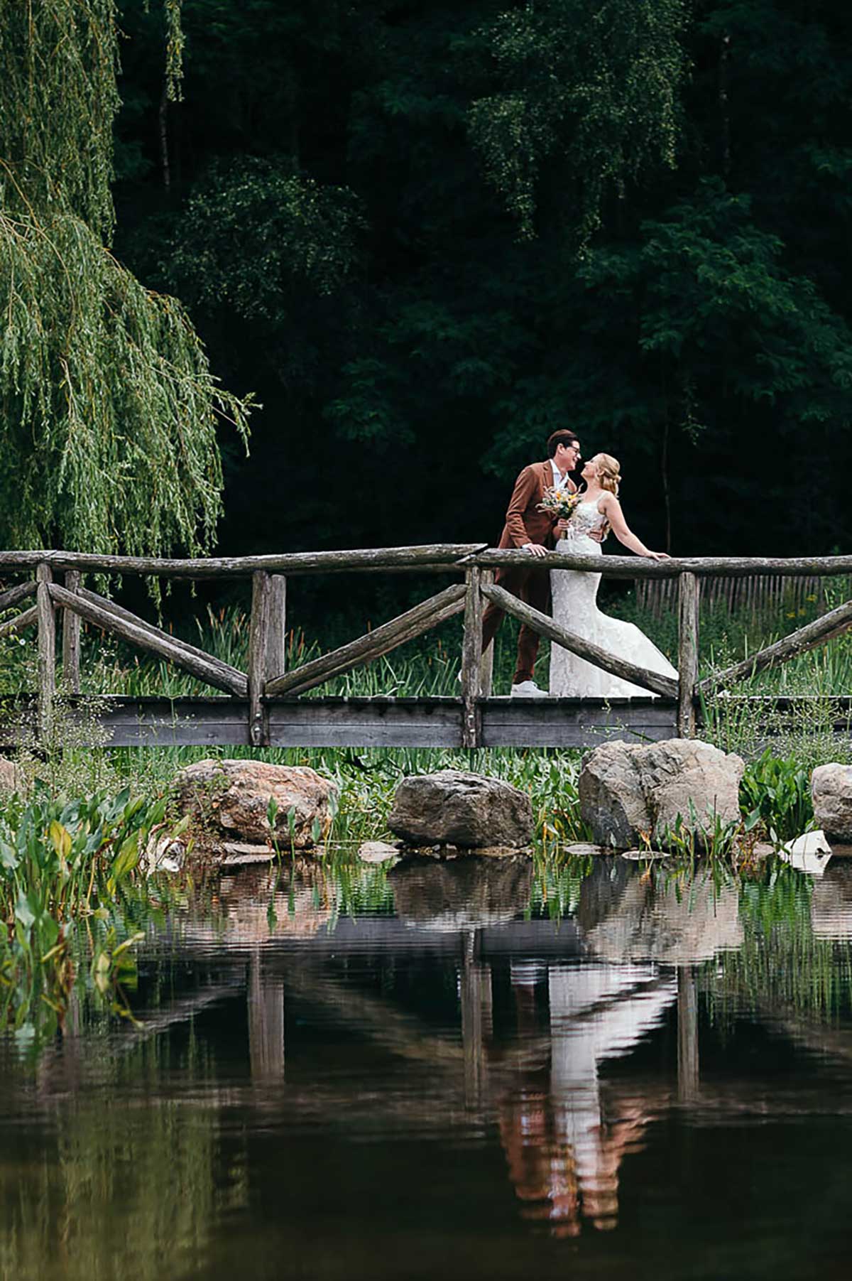 Prachtig bruidspaar staat elegant op een schilderachtig bruggetje over een rustige rivier in het idyllische Warredal.
